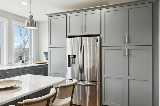 kitchen with a breakfast bar, gray cabinets, hanging light fixtures, light stone countertops, and stainless steel fridge with ice dispenser