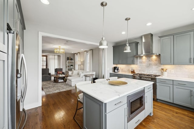 kitchen featuring gray cabinets, backsplash, appliances with stainless steel finishes, open floor plan, and wall chimney exhaust hood