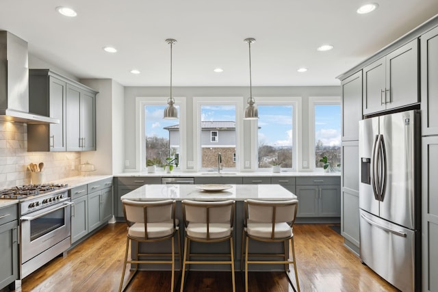 kitchen featuring wall chimney exhaust hood, appliances with stainless steel finishes, gray cabinets, light wood-type flooring, and backsplash