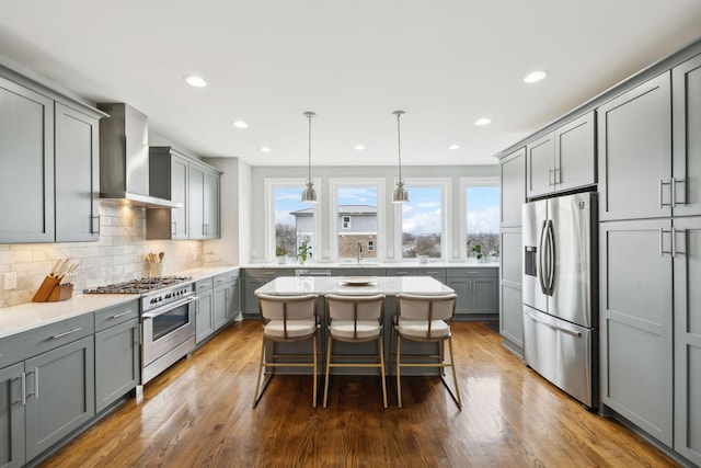 kitchen with wall chimney range hood, stainless steel appliances, a sink, and gray cabinetry