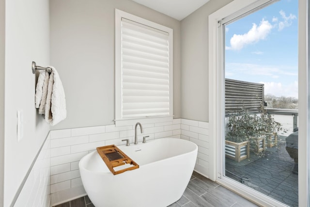 bathroom featuring wood tiled floor, a freestanding tub, wainscoting, and tile walls