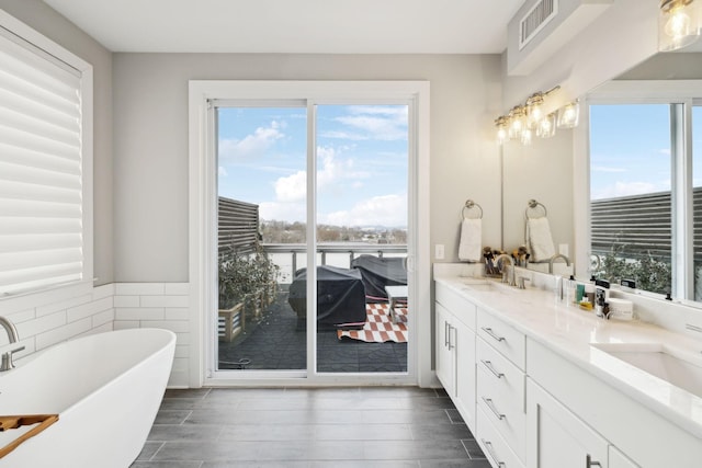 full bath featuring double vanity, a freestanding bath, visible vents, and a sink