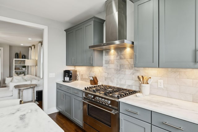 kitchen featuring dark wood-style flooring, stainless steel range, backsplash, gray cabinetry, and wall chimney exhaust hood