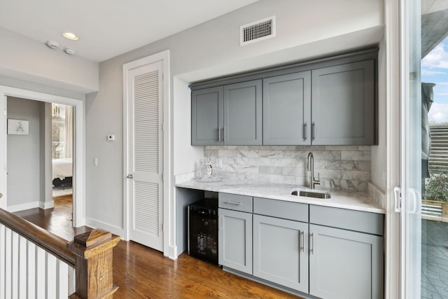 bar featuring beverage cooler, dark wood-type flooring, a sink, visible vents, and decorative backsplash