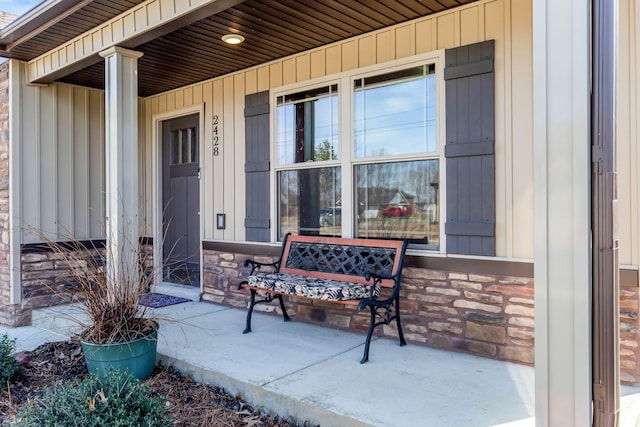 doorway to property with covered porch, stone siding, and board and batten siding