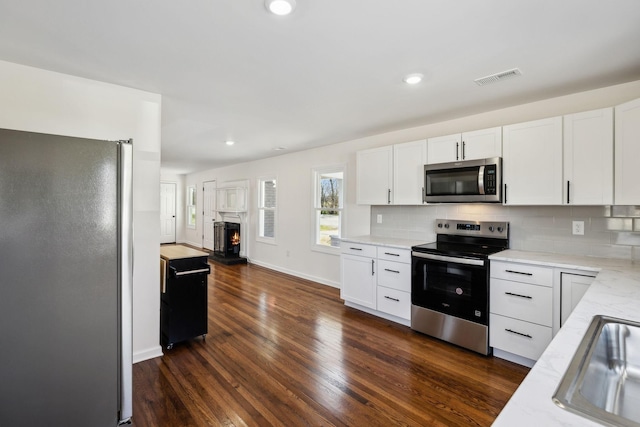 kitchen featuring stainless steel appliances, visible vents, white cabinets, decorative backsplash, and dark wood finished floors