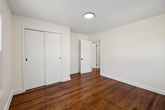 unfurnished bedroom with dark wood-type flooring, a closet, and baseboards