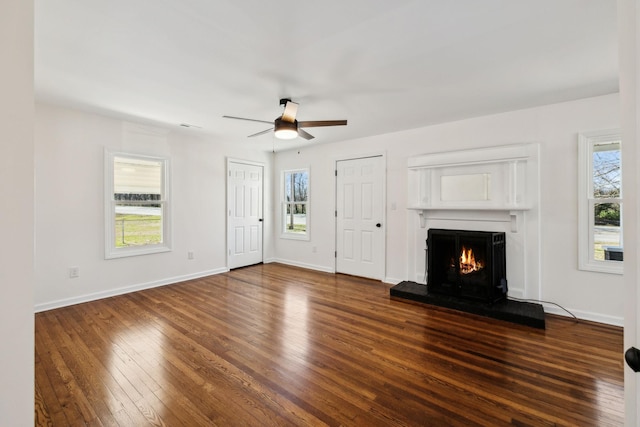 unfurnished living room with dark wood-style flooring, a healthy amount of sunlight, a lit fireplace, and baseboards