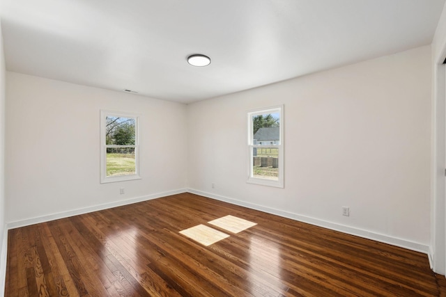 empty room with dark wood-style floors, visible vents, and baseboards