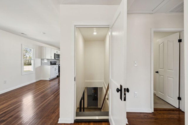 hall with dark wood-type flooring, visible vents, and baseboards