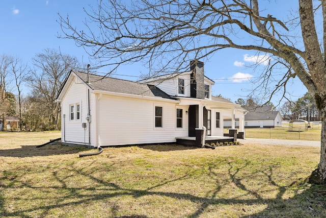 view of side of property featuring a chimney, a lawn, and roof with shingles