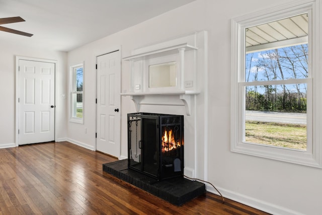 unfurnished living room featuring dark wood-style floors, a wealth of natural light, a warm lit fireplace, and baseboards