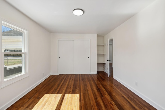 unfurnished bedroom with dark wood-type flooring, a closet, and baseboards