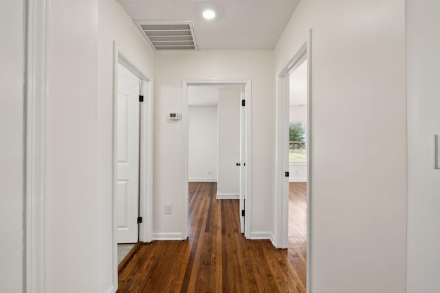 corridor featuring dark wood-type flooring, visible vents, and baseboards