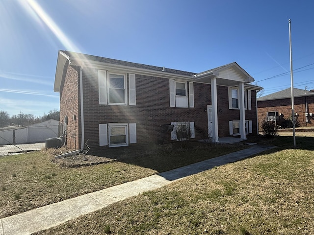 raised ranch with central AC unit, brick siding, fence, and a front yard