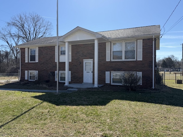 raised ranch with a front yard, fence, and brick siding