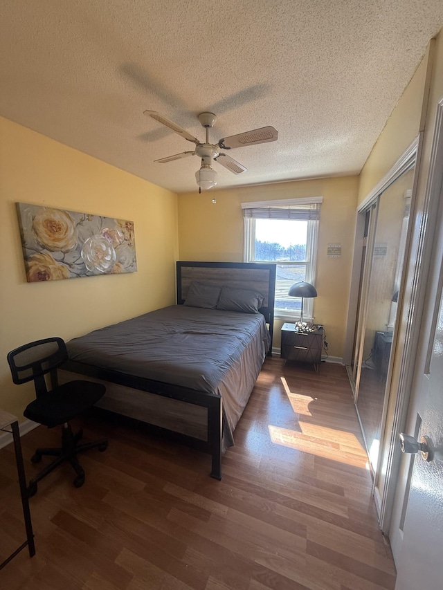 bedroom featuring a closet, a ceiling fan, a textured ceiling, wood finished floors, and baseboards