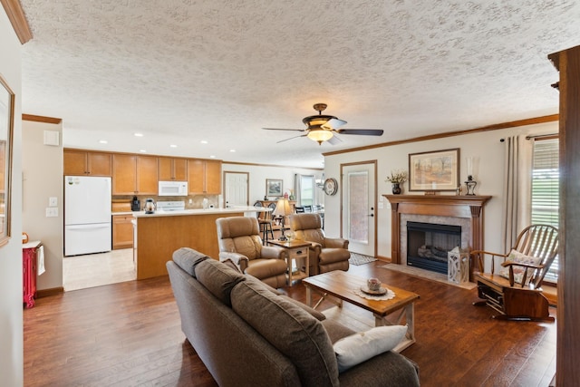 living room with dark wood-style floors, ceiling fan, crown molding, a textured ceiling, and a fireplace