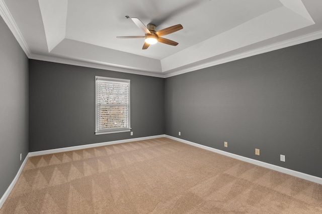 carpeted spare room with ornamental molding, a tray ceiling, and baseboards