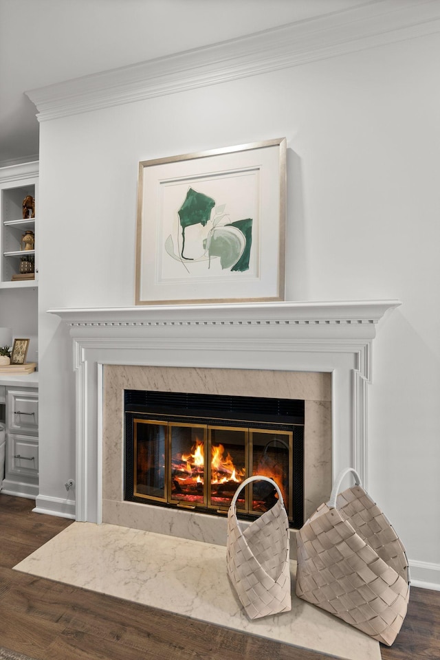 interior details with a premium fireplace, baseboards, crown molding, and wood finished floors