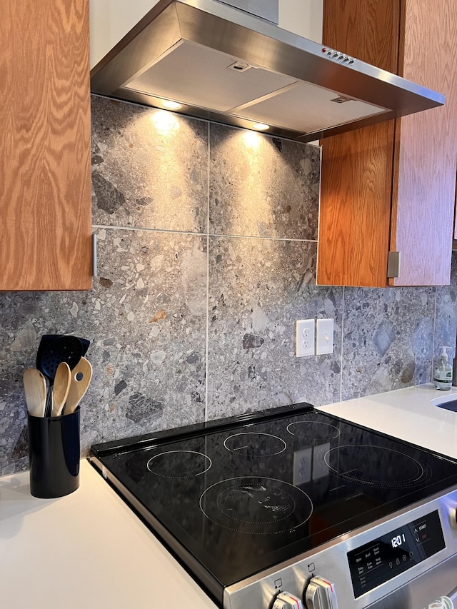 kitchen featuring stainless steel electric range oven, tasteful backsplash, brown cabinetry, and range hood