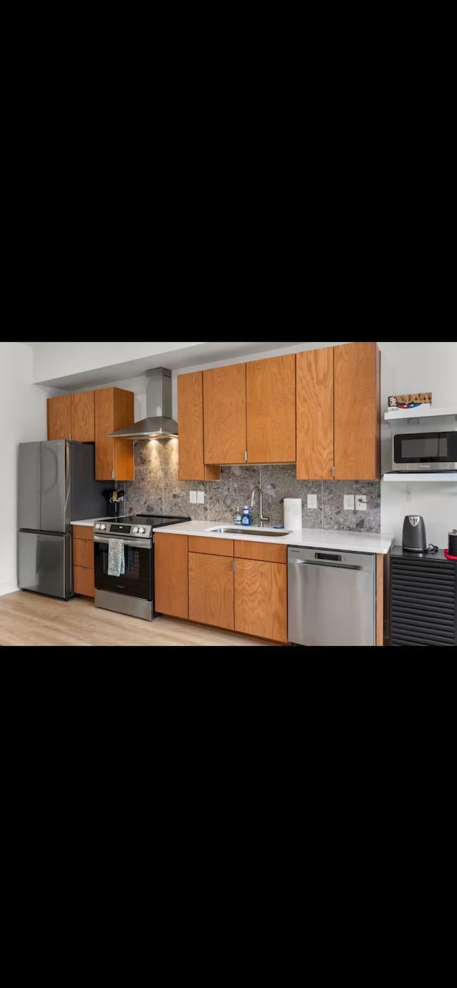 kitchen featuring light countertops, decorative backsplash, appliances with stainless steel finishes, a sink, and wall chimney range hood