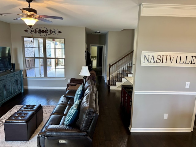 living area with dark wood-type flooring, ceiling fan, baseboards, and stairs