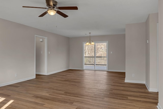 spare room with ceiling fan with notable chandelier, baseboards, and wood finished floors