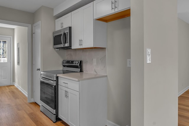 kitchen with light wood finished floors, white cabinets, decorative backsplash, appliances with stainless steel finishes, and light countertops