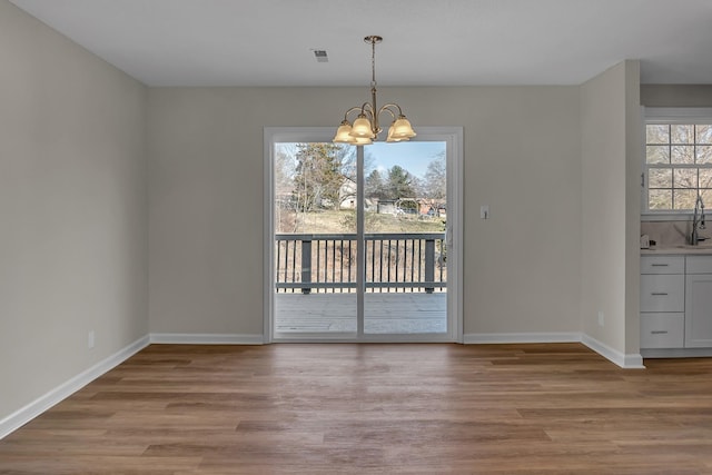 unfurnished dining area with a chandelier, visible vents, baseboards, and wood finished floors