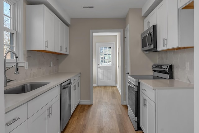 kitchen featuring appliances with stainless steel finishes, light wood-style floors, white cabinetry, a sink, and baseboards