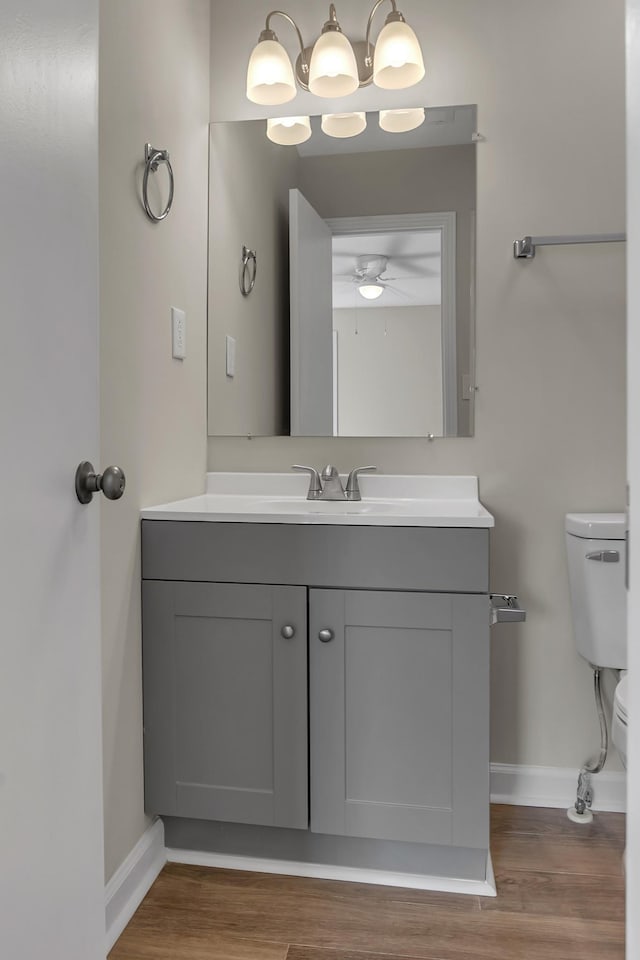 half bath featuring toilet, ceiling fan, vanity, wood finished floors, and baseboards