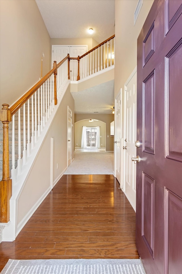 entrance foyer with baseboards, visible vents, a towering ceiling, stairway, and wood finished floors