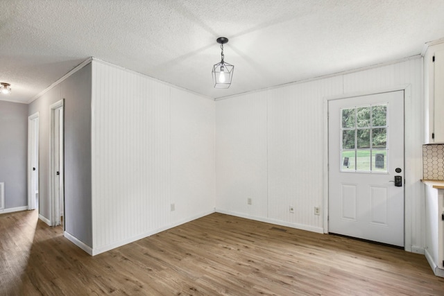 unfurnished dining area with a textured ceiling, ornamental molding, wood finished floors, and baseboards