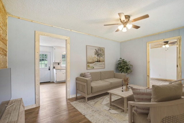 living area with a textured ceiling, ceiling fan, ornamental molding, and wood finished floors