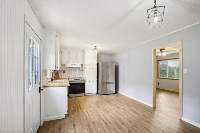 kitchen with under cabinet range hood, stainless steel appliances, a sink, white cabinets, and crown molding