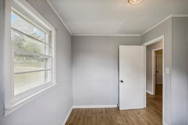 empty room featuring ornamental molding, a textured ceiling, baseboards, and wood finished floors