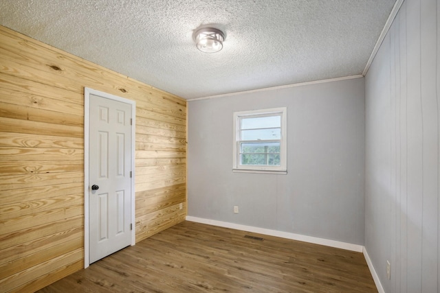 spare room featuring wooden walls, a textured ceiling, visible vents, and wood finished floors