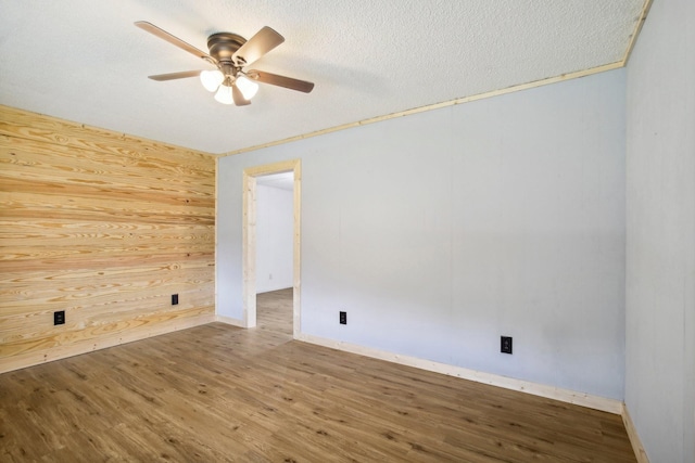 spare room with a textured ceiling, wood walls, wood finished floors, and a ceiling fan