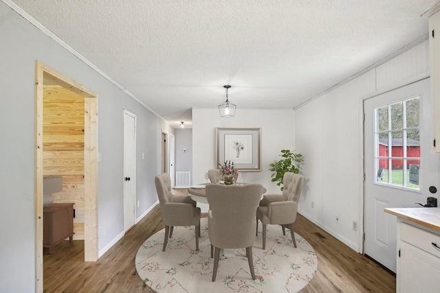 dining space featuring a textured ceiling, wood finished floors, visible vents, baseboards, and crown molding