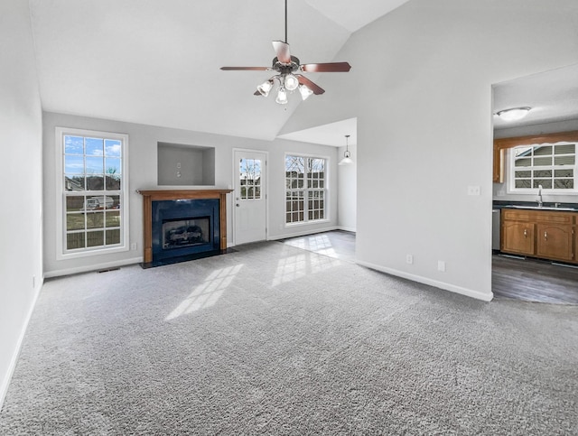 unfurnished living room with carpet floors, plenty of natural light, a fireplace with flush hearth, and a sink