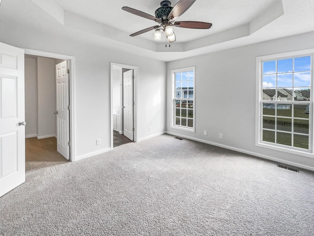 unfurnished bedroom featuring a tray ceiling, carpet, visible vents, ceiling fan, and baseboards