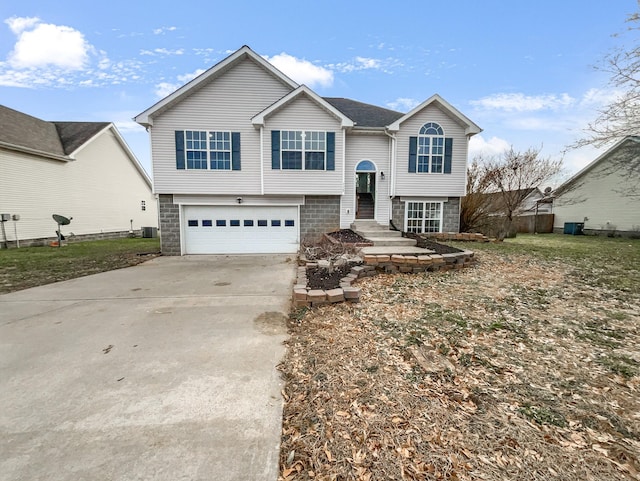 bi-level home featuring concrete driveway, an attached garage, and central AC unit