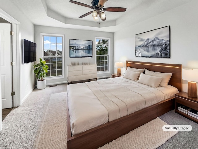 carpeted bedroom with visible vents, multiple windows, a tray ceiling, and baseboards