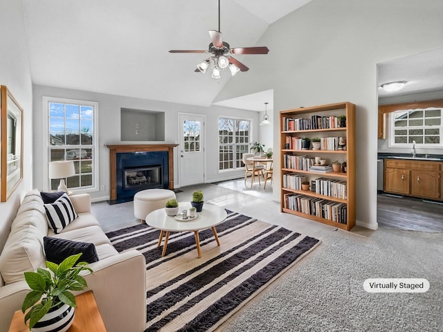 carpeted living room featuring a fireplace with flush hearth, a wealth of natural light, a sink, and high vaulted ceiling