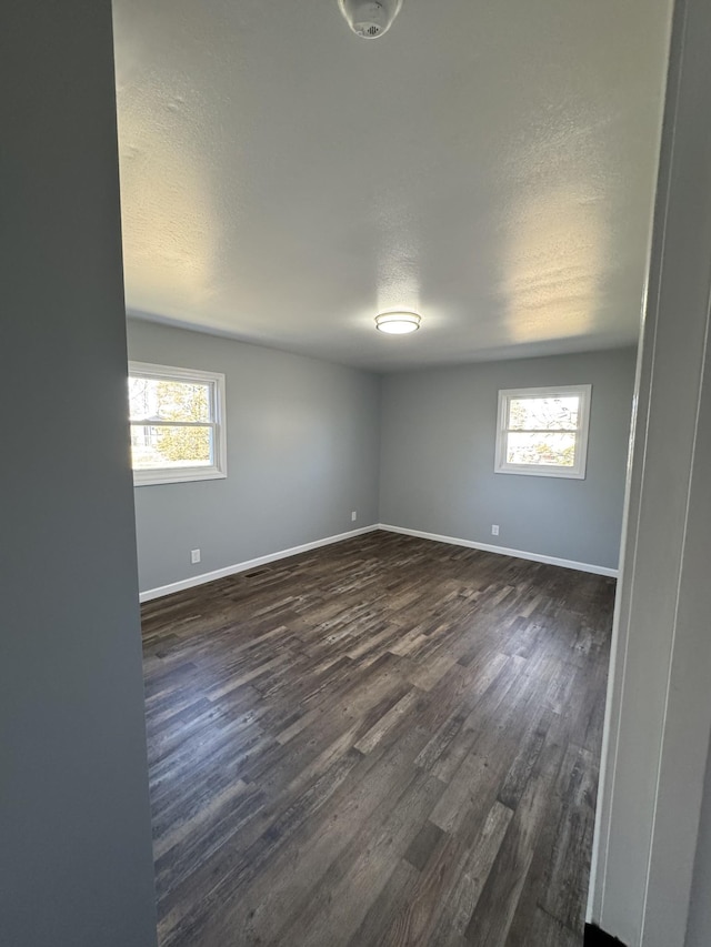 unfurnished room with a textured ceiling, baseboards, dark wood finished floors, and a wealth of natural light