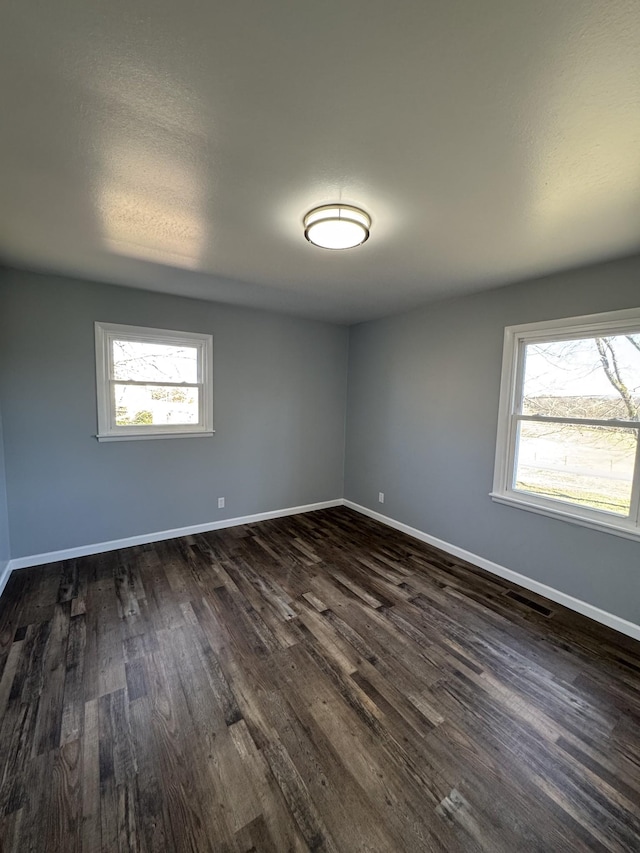 spare room featuring dark wood finished floors, visible vents, plenty of natural light, and baseboards