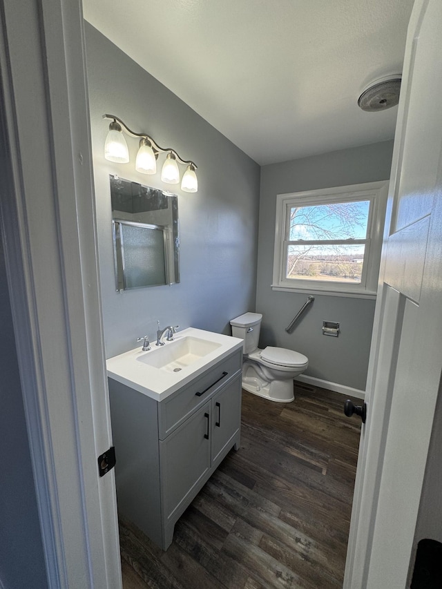 bathroom featuring toilet, a shower stall, vanity, wood finished floors, and baseboards