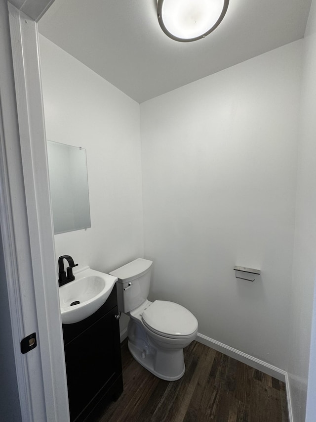 half bathroom featuring toilet, baseboards, wood finished floors, and vanity