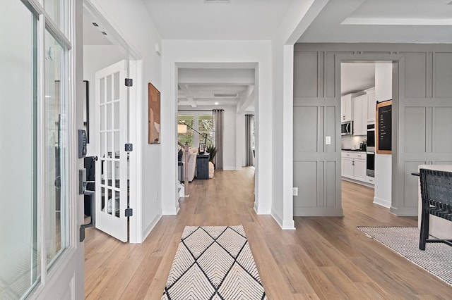 foyer entrance featuring beam ceiling, coffered ceiling, light wood-style flooring, and baseboards